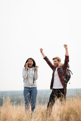 Smiling traveler showing yes gesture near african american girlfriend talking on smartphone outdoors