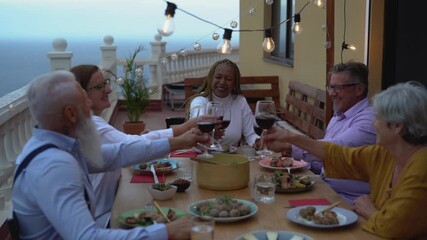 Happy multiracial seniors toasting with red wine glasses together on house patio dinner - Powered by Adobe