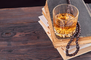 Glass cup with alcohol on a stack of books. Brown rustic wooden table.