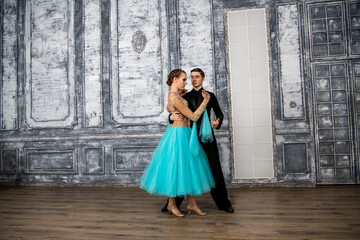 a young man in a black suit is dancing with a girl in a turquoise dress in the dance hall