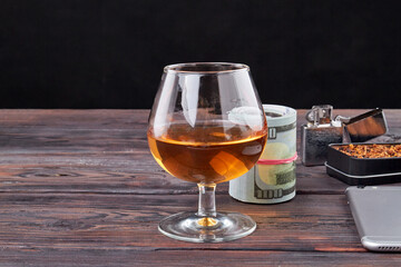 Unhealthy lifestyle concept. Still life composition of glass of cognac and money bundle.