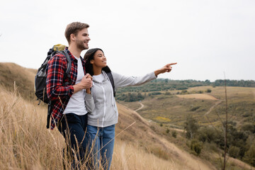 Smiling african american woman pointing with finger near boyfriend during trip with backpacks