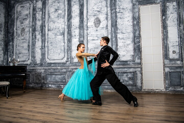 a young man in a black suit is dancing with a girl in a turquoise dress in the dance hall