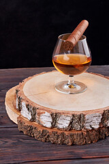 Vertical shot glass of brandy and cuban cigar. Round wooden board.