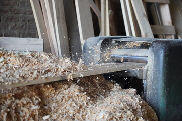 Working at Wood planing machine working. Sawmill, business and wood factory for construction. Heavy machine planing wood. Mountains of sawdust.