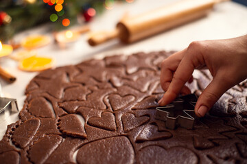 Close up photo of a flat rolled dough shaped in different forms. Christmas decorations and a rolling pin on the bckground