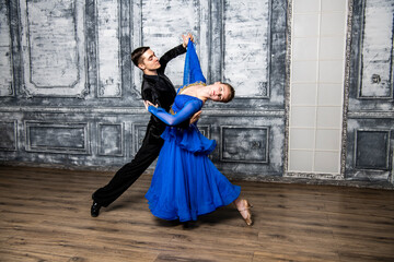 young man dancing with a girl in a blue ballroom dress in a gray dance hall