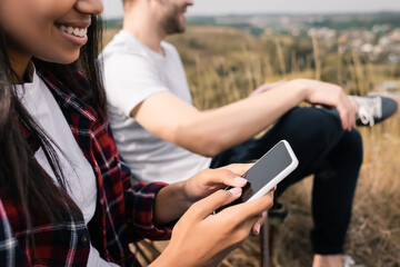 Cropped view of smiling african american woman using smartphone near boyfriend on blurred background during camping