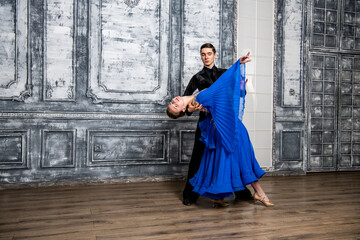 young man dancing with a girl in a blue ballroom dress in a gray dance hall
