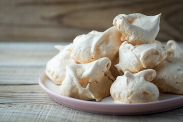 Homemade meringue cookies on a plate, on a wooden table by the window, closeup. Italian, French sweet dessert made of eggs and sugar, natural light.