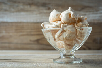 Homemade meringue cookies, beautifully arranged in a transparent glass crematorium, on a wooden table by the window, closeup. Italian, French sweet dessert made of eggs and sugar, natural light.