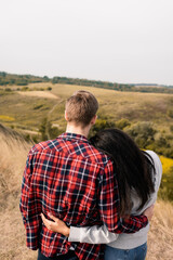 Back view of multiethnic couple hugging with hills on blurred background