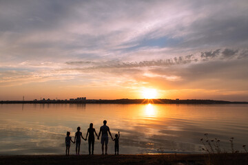 Silhouettes of family standing on sea beach together and looking at sunset