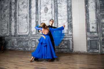 Fototapeta premium young man dancing with a girl in a blue ballroom dress in a gray dance hall