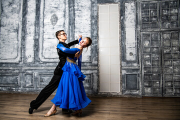 Naklejka premium young man dancing with a girl in a blue ballroom dress in a gray dance hall
