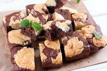 Chocolate brownie square pieces with cookies, decorated with mint leaves on a wooden table