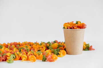 Multicolored pasta in a disposable kraft paper cup scattered on a white background. Copy, empty space for text