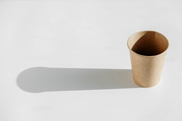 Disposable paper cup with shadow from light on a white background. Copy, empty space for text