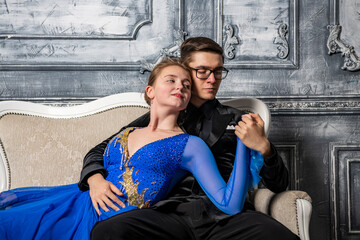 young couple in evening dresses sitting on a white couch in the dance hall