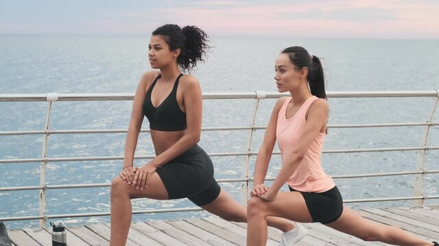 Young amazing sports women making stretching exercise outdoors at the beach together
