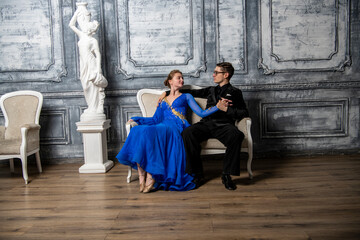 young couple in evening dresses sitting on a white couch in the dance hall