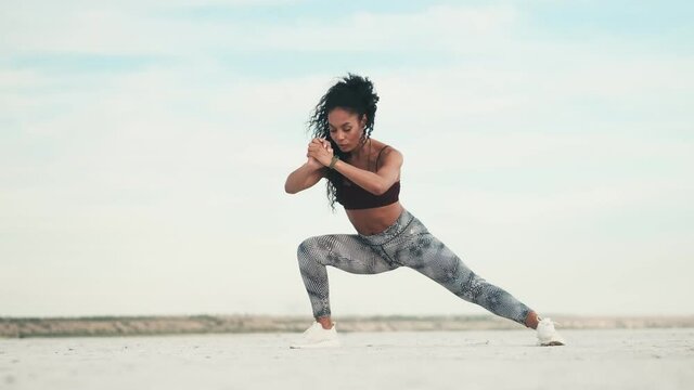 A focused african american woman wearing sportswear is doing exercises outside at the beach