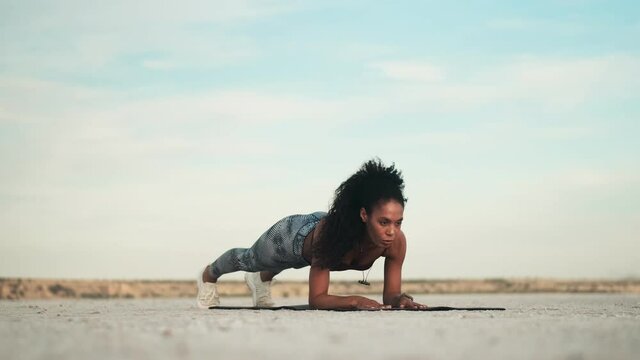 A strong young african american woman wearing sportswear is doing exercises on the yoga mat outside at the beach