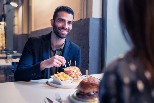 Portrait of a bearded young man eating chips and sandwiches in an outdoor restaurant. Concept of romance and couples enjoying free time together. - Powered by Adobe