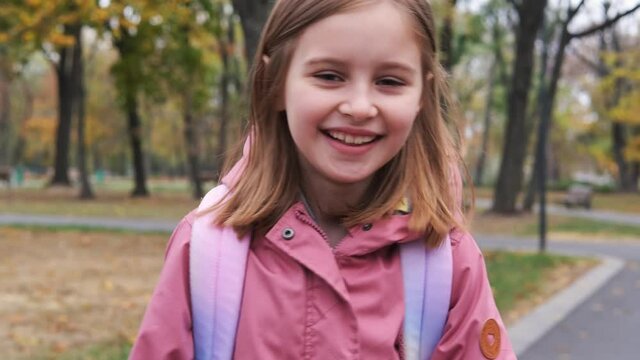 Smiling little girl with backpack walking after school in autumn park