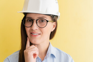 Portrait of smiling beautiful tatar woman engineer in construction helmet and glasses isolated on yellow background
