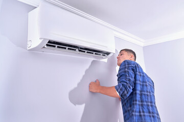 A man inspects the air conditioner at home, checks if it works