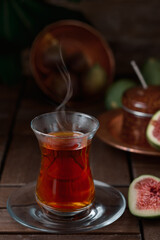Tea in a traditional armudu glass, half a ripe fig next to it. Dessert in the background - fig jam. vintage wooden table, close-up