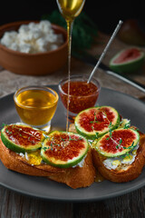 Honey dripping from a spoon onto fig sandwiches on toasted goat cheese baguette on a plate with honey, sesame seeds and walnuts. Fresh toast with figs and garnished with thyme leaves. Close-up
