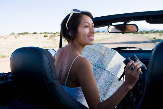 Native American woman in sun dress looking at a map in the passenger seat of a convertible.