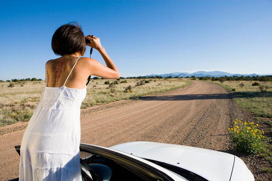 Native American woman in sun dress driving a white convertible sports car on desert dirt road