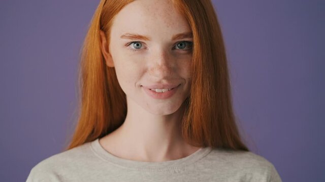 A close-up view of an attractive young woman is opening her eyes and looking to the camera standing isolated over a violet background