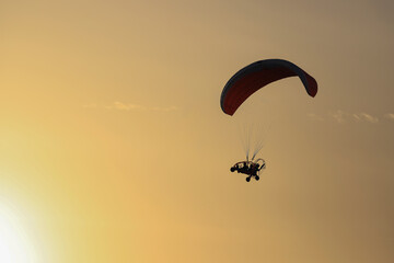 Paraglider in flight, against the background of the sky and clouds colored orange by the setting sun