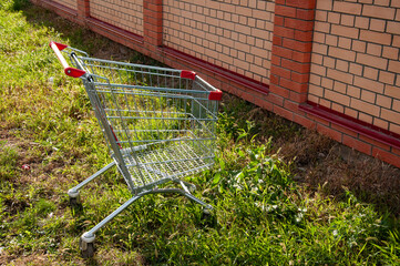 an empty cart from the supermarket stands on the lawn near a brick fence.
