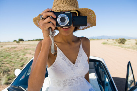 Native American woman in sun dress sitting on white convertible sports car,taking pictures