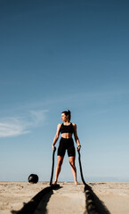 Fit and toned sportswoman working out in functional training gym at the beach - Battle ropes...