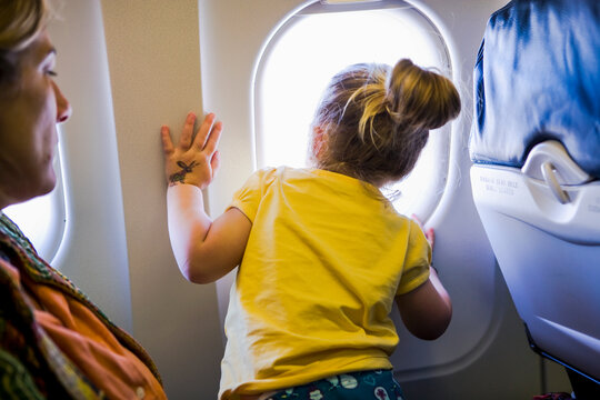 young girl looking out window of airplane