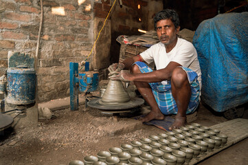 Indian potter making small pot or Diya for Diwali with clay on potters wheel in his small factory. Manufacturing traditional handicraft with clay.