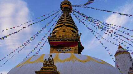 Front view of the top of golden colored Buddhist stupa in temple complex Swayambhunath, Kathmandu, Nepal decorated with colorful prayer flags flying in the wind.