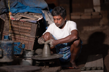 Indian potter making small pot or Diya for Diwali with clay on potters wheel in his small factory.Handwork craft.