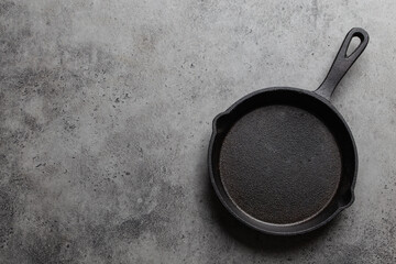 Empty vintage black cast-iron frying pan on rustic stone background, top view. Cooking concept backdrop with space for text from above