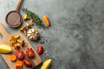 Fresh cherry tomatoes, potatoes, mushrooms chanterelles, carrot, herbs on cutting board and wooden cooking spoon with olive oil. Food cooking background with ingredients, top view, space for text