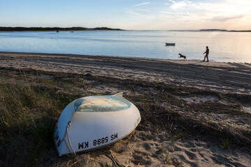 An upside boat on beach with man walking dog in Wellfleet, MA