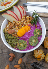 Healthy breakfast Purple smoothie bowl: An apple fruit smoothie with banana, coconut, almonds, sunflower and chia seeds and kiwi