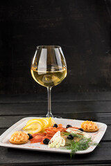 glass of white wine with fish platter snack on black background
