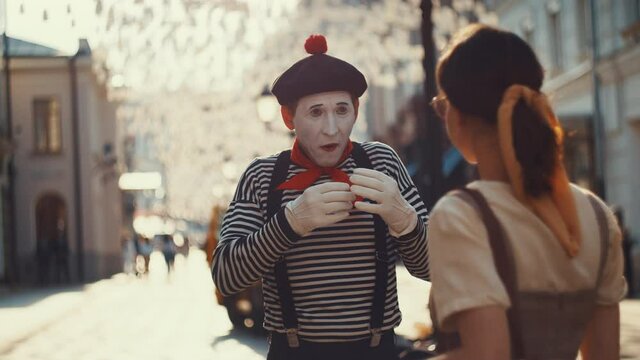 Young mime giving a heart to young girl outdoors
